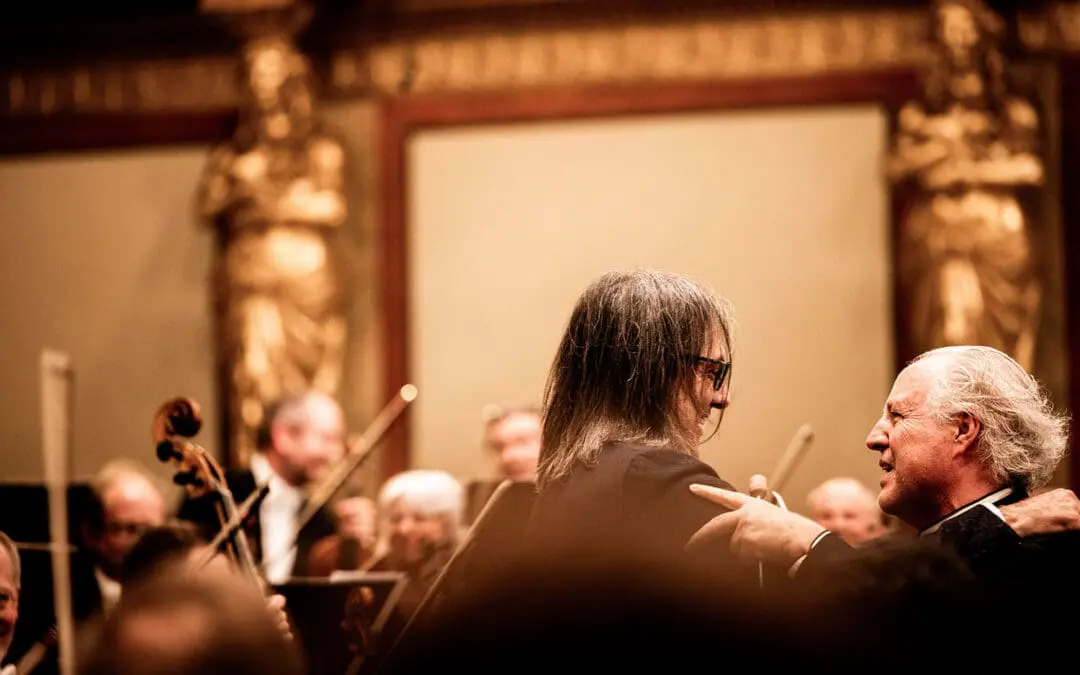 Violinist Leonidas Kavakos und Dirigent Manfred Honeck umarmen sich auf der Bühne, im Hintergrund sind die Wiener Symphoniker zu sehen